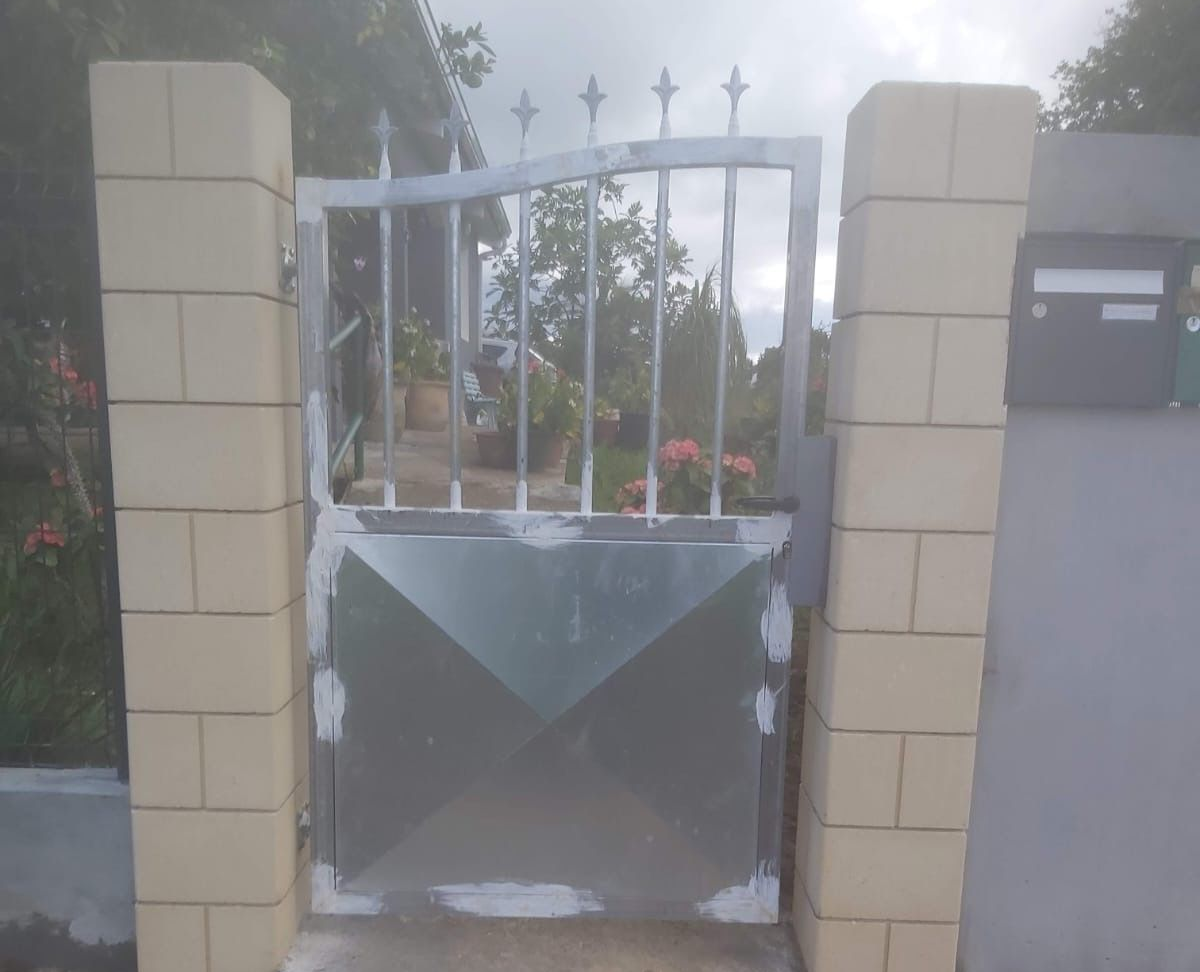 Portail métallique à motif géométrique, encadré par des piliers en briques, avec une boîte aux lettres à droite.