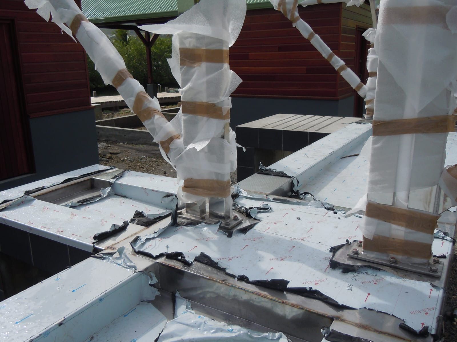 Ossature métallique avec colonnes de soutien enveloppées sur une structure partiellement construite, montrant un revêtement protecteur déchiré.