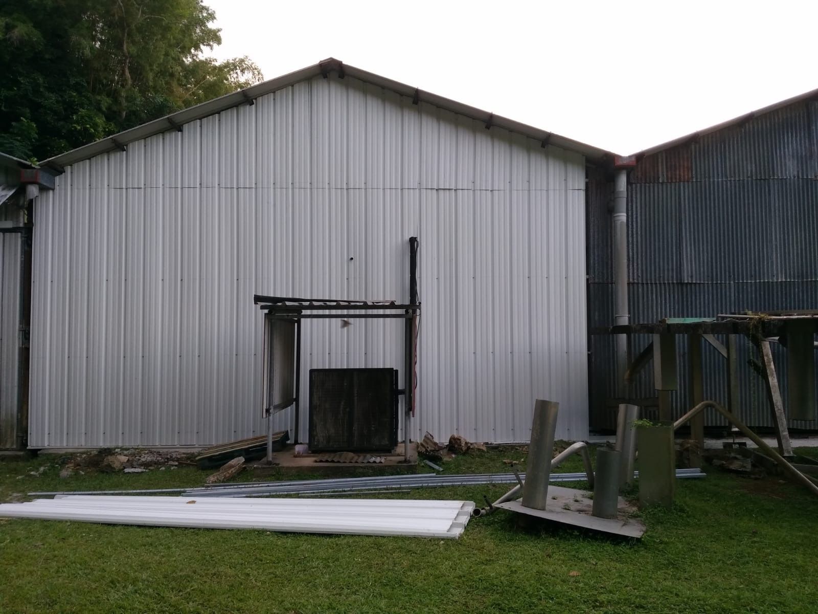 Abri de jardin à parois métalliques avec porte ouverte, situé dans une zone herbeuse, entouré de chutes de bois et d'outils.