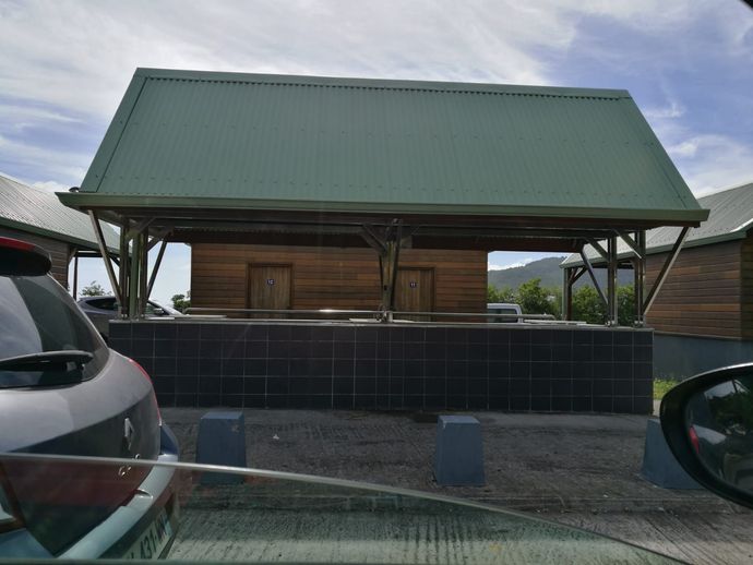 Structure en bois avec toit vert, surplombant un mur carrelé sombre. Des voitures sont garées devant.