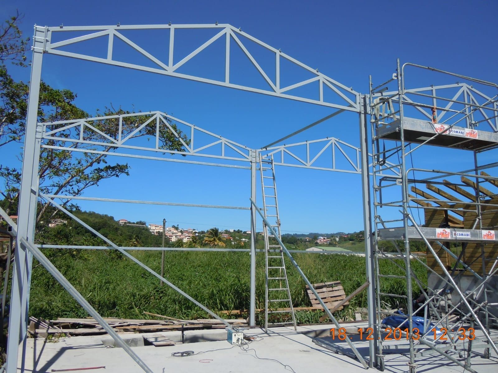 Construction à ossature métallique d'un bâtiment sous un ciel bleu, avec des échafaudages sur la droite.