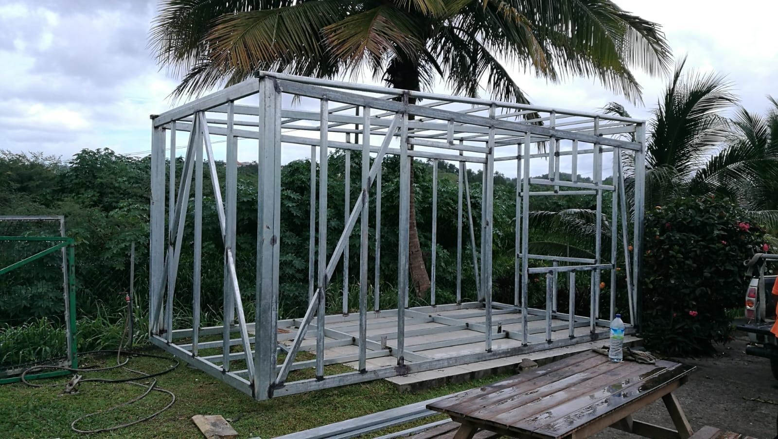 Structure métallique d'un petit bâtiment en construction à l'extérieur, entourée de verdure.