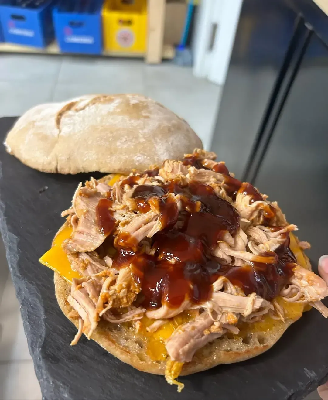 Un sándwich de cerdo desmenuzado con queso y salsa barbacoa en un pan.
