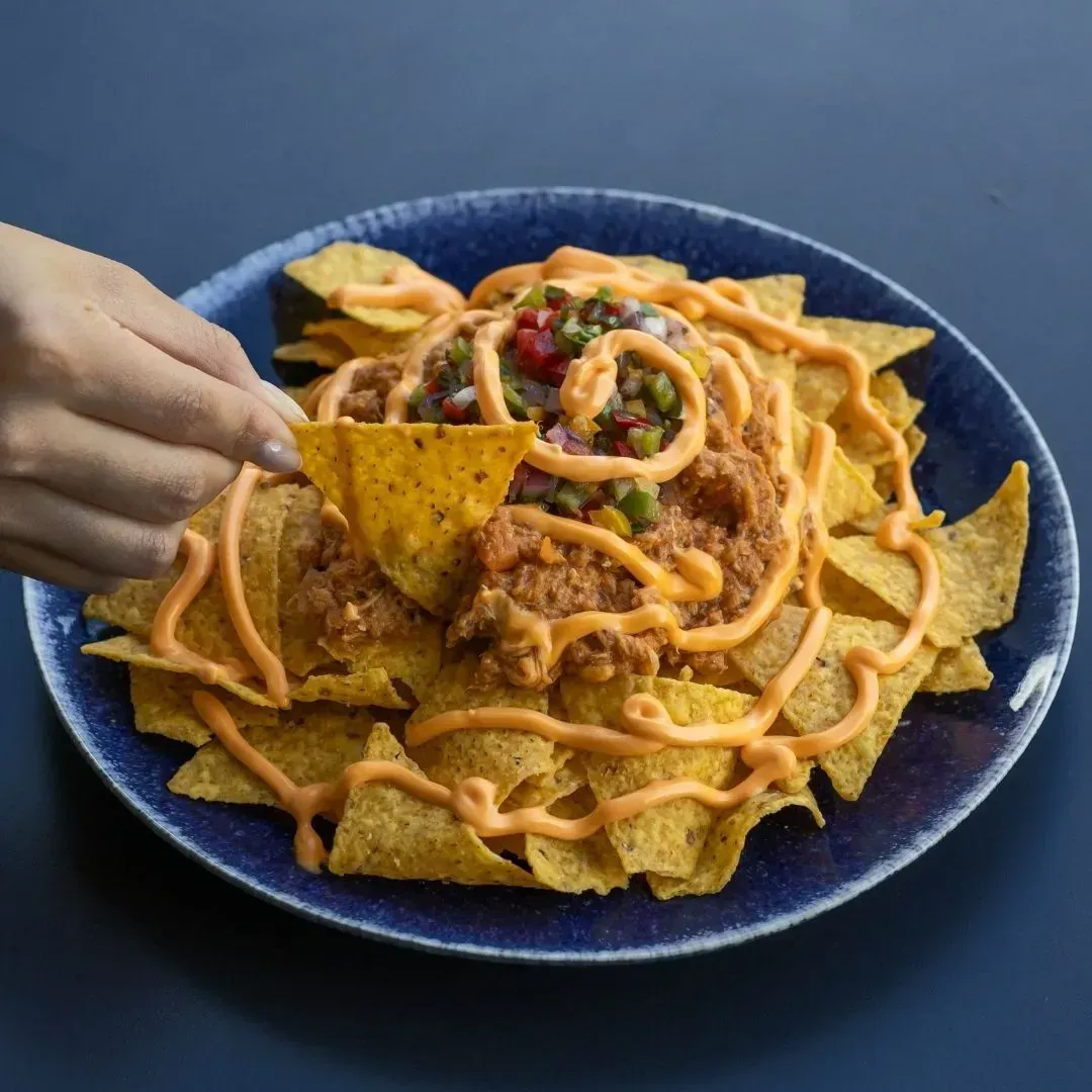 Una persona está sacando un totopo de un plato de nachos.