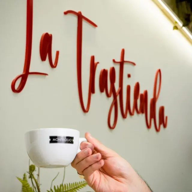 Una persona sostiene una taza frente a un cartel que dice