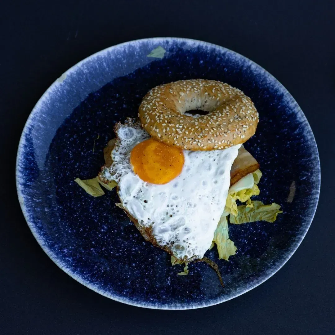 Un plato azul cubierto con un huevo frito y un bagel.