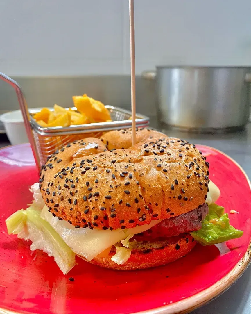 Una hamburguesa está sentada en un plato rojo al lado de una canasta de papas fritas.