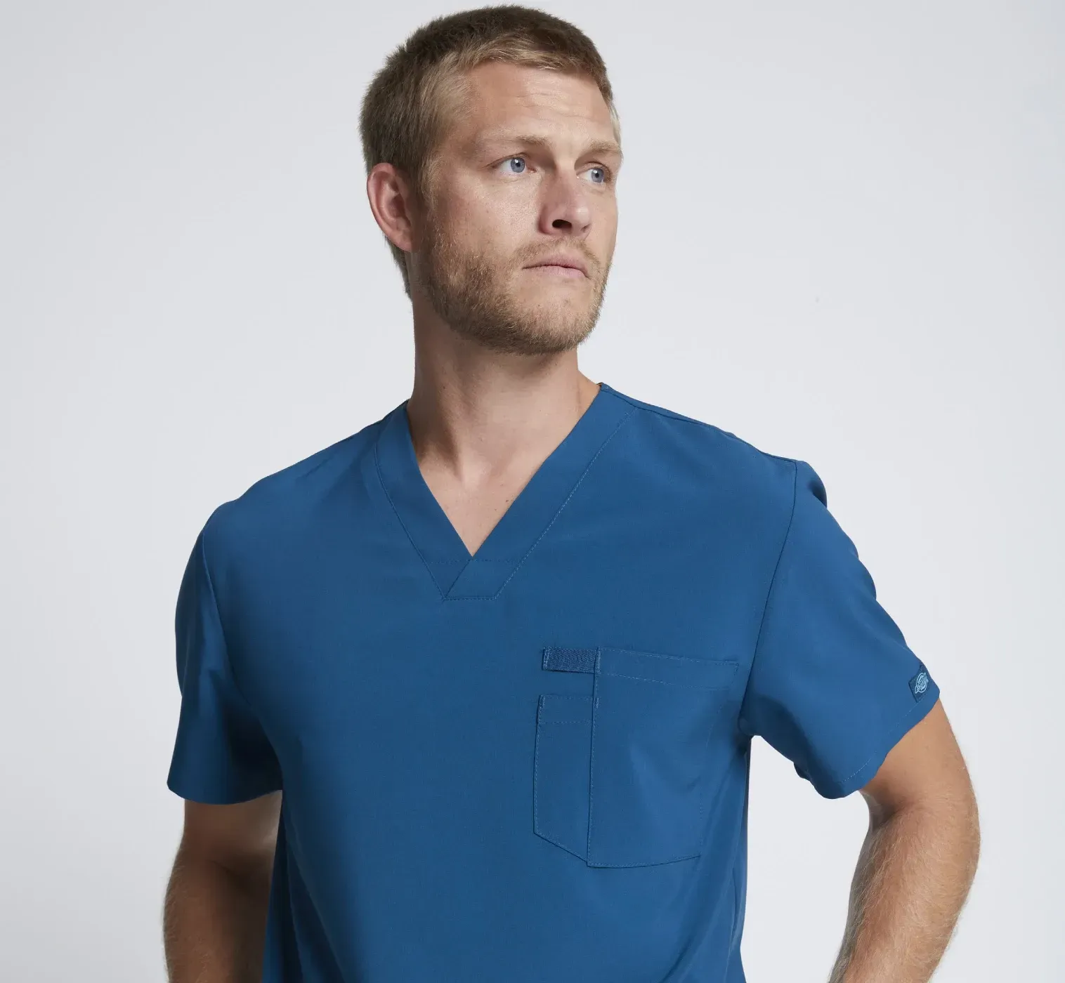 Un hombre que viste una camiseta azul está de pie con las manos en los bolsillos.