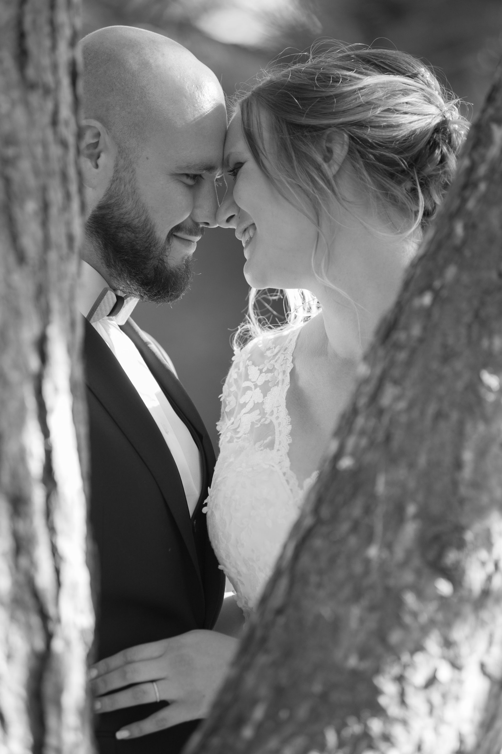 Mariés en noir et blanc derrière un arbre