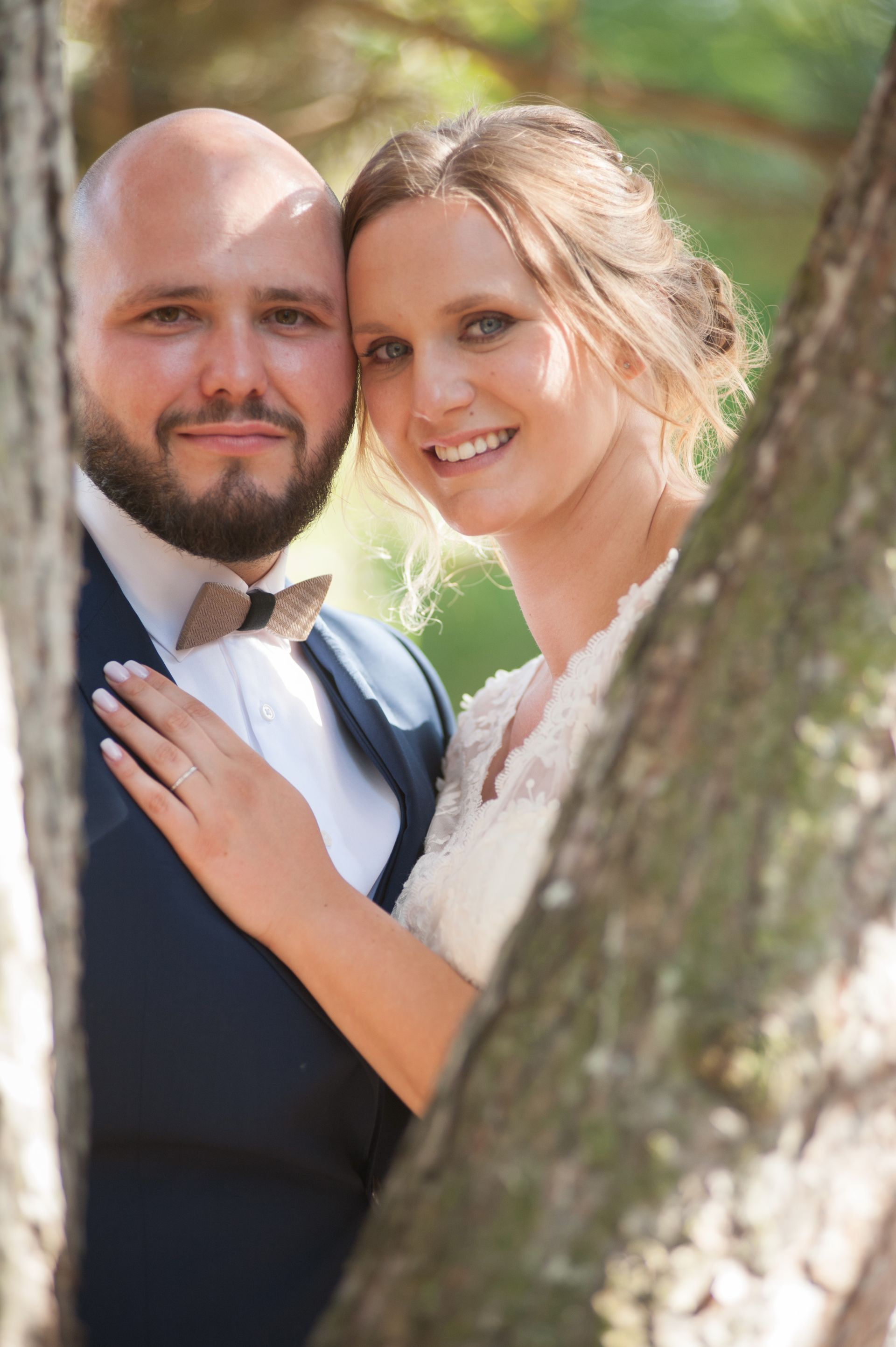 Mariés psoant derrière un arbre