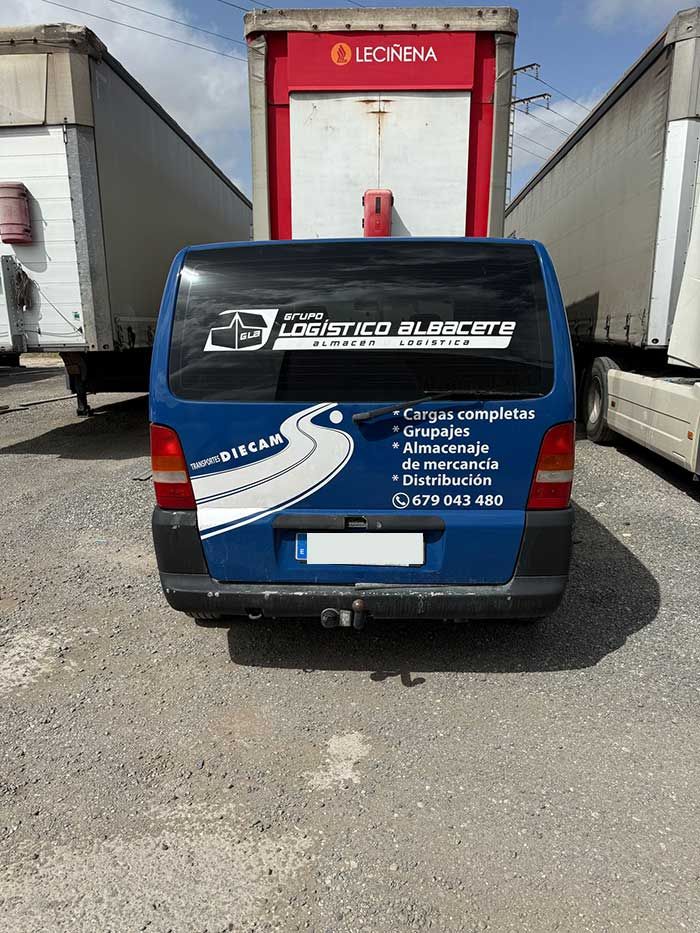 Una camioneta azul está estacionada en un estacionamiento al lado de un camión.