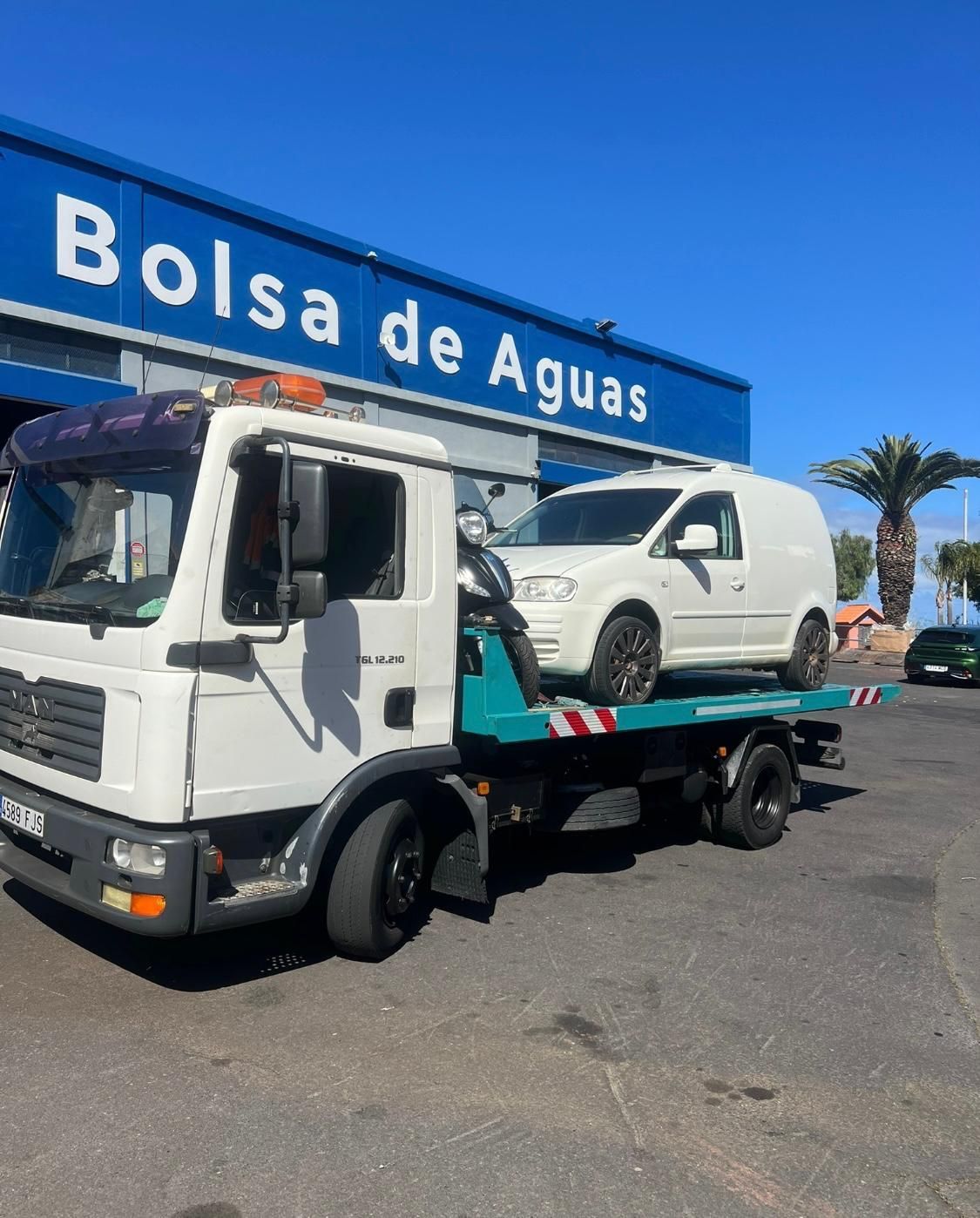 Una grúa con dos coches en la parte trasera está estacionada frente a Bolsa de Aguas.