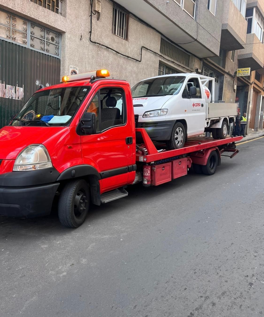 Una grúa roja transporta un coche blanco en la parte trasera.