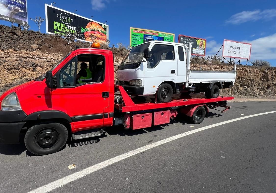 Una grúa roja está remolcando un camión blanco por una carretera.