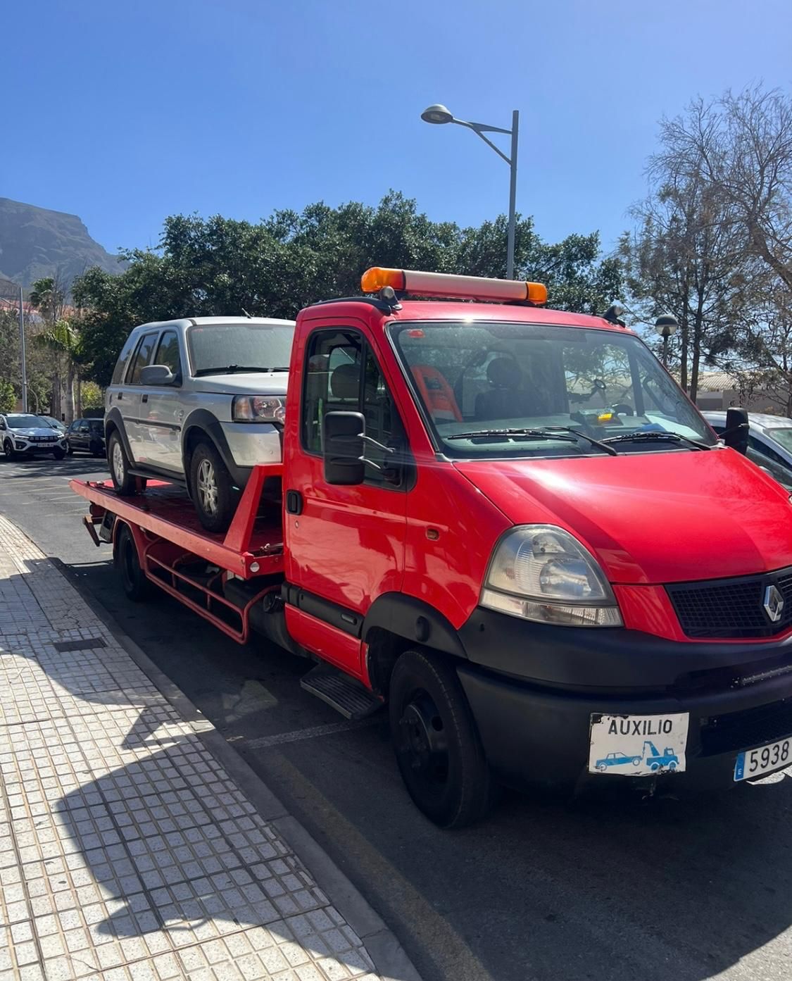 Una grúa roja con una furgoneta en la parte trasera está estacionada al costado de la carretera.