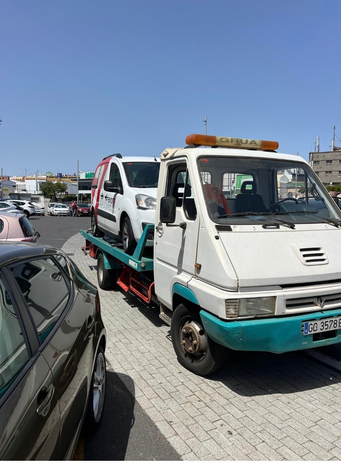 Una grúa transporta dos coches en un estacionamiento.