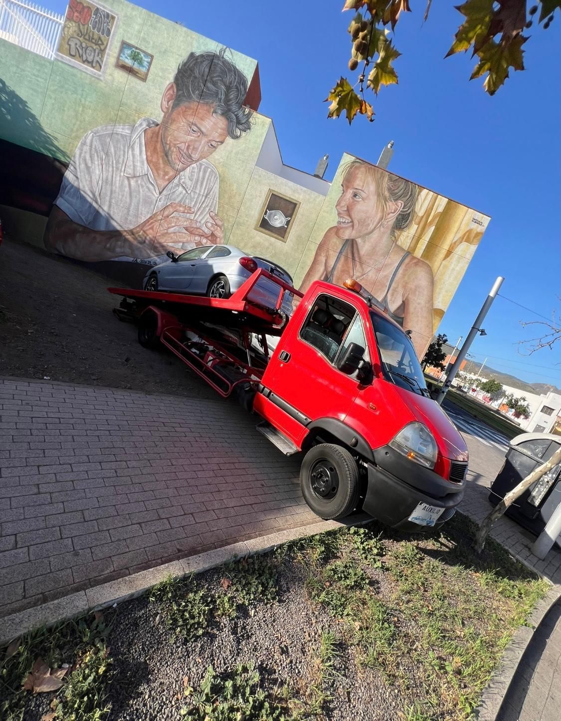 Una grúa roja está estacionada frente a un mural de un hombre y una mujer.
