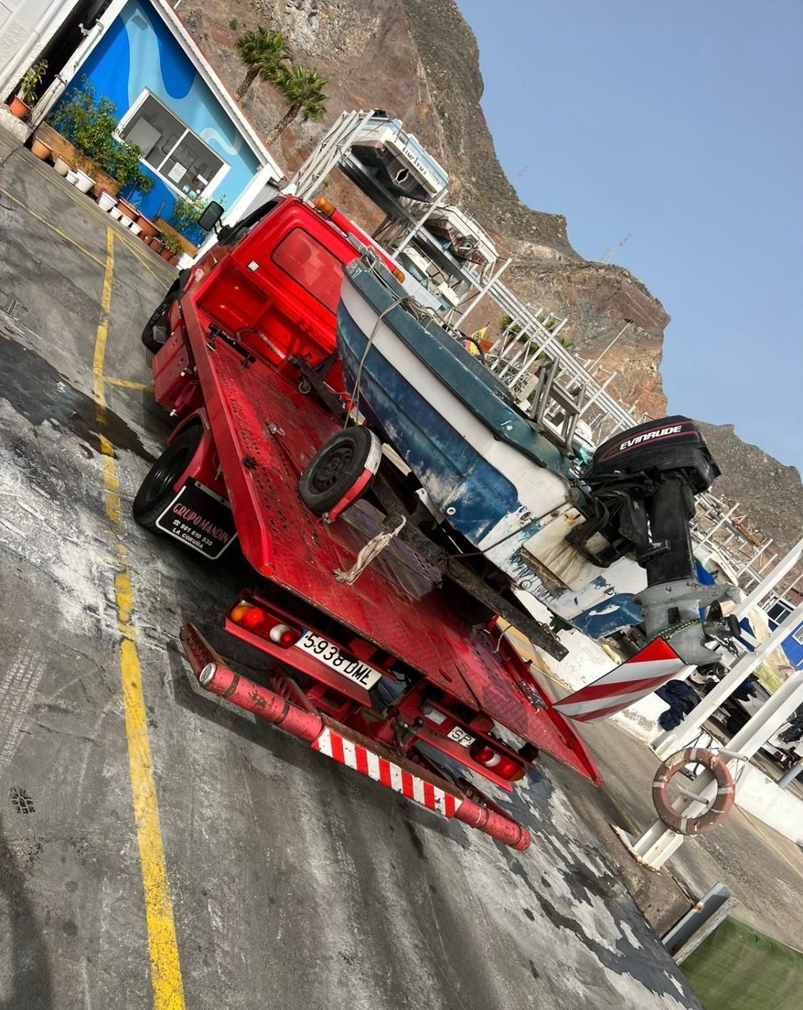 Una grúa roja transporta un barco en la parte trasera.