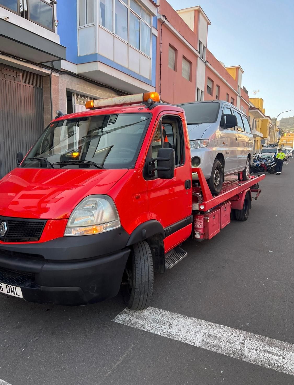 Una grúa roja transporta una furgoneta blanca por una calle.