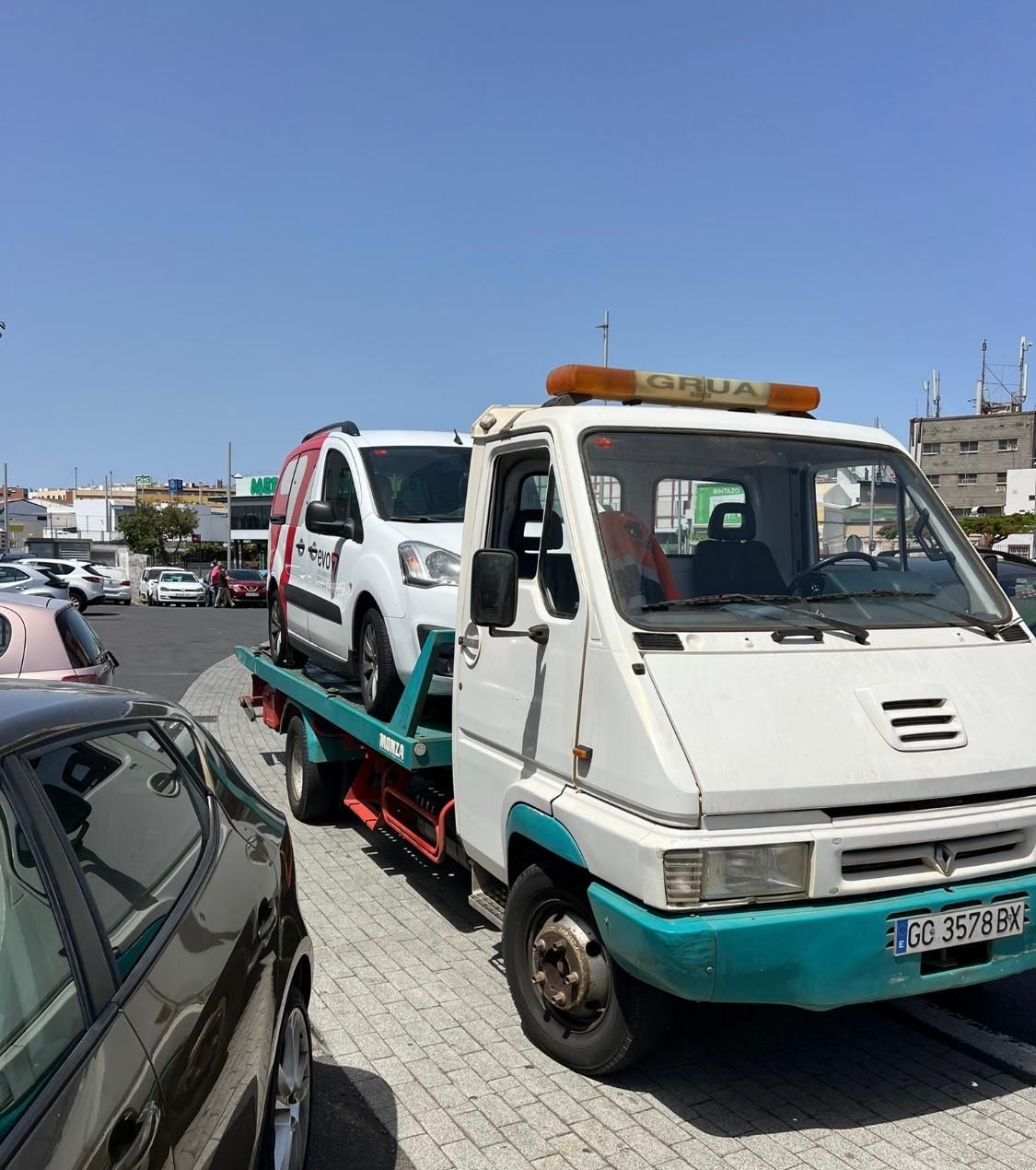 Una grúa transporta un automóvil en un remolque en un estacionamiento.
