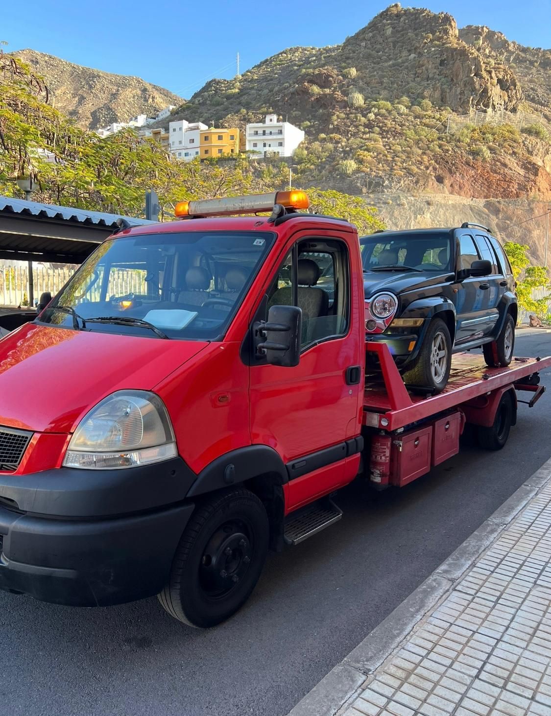 Una grúa roja con un jeep en la parte trasera.