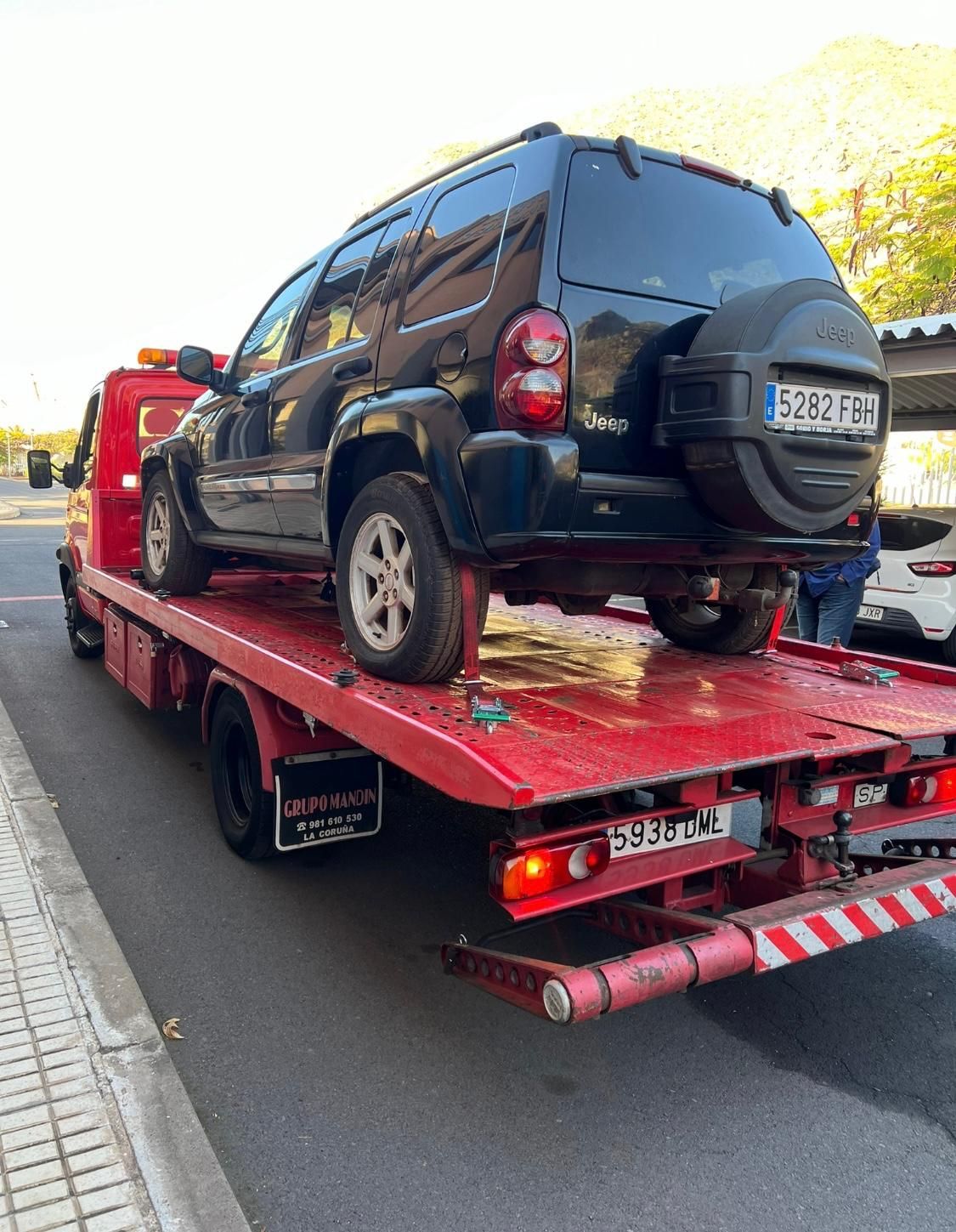 Un jeep negro está sentado encima de una grúa roja.