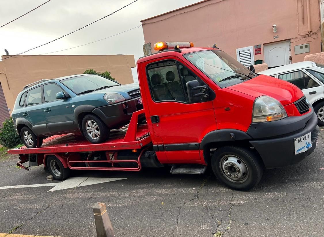 Una grúa roja transporta dos coches en la parte trasera.