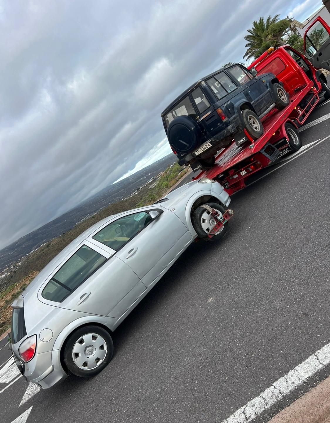 Un coche plateado está siendo remolcado por una grúa roja.