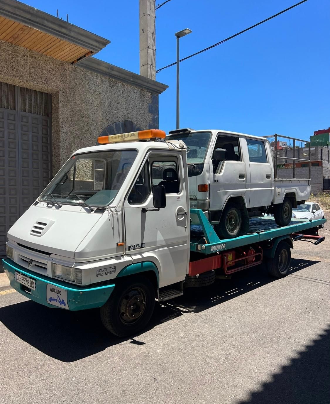 Una grúa blanca con dos coches en la parte trasera está estacionada al costado de la carretera.