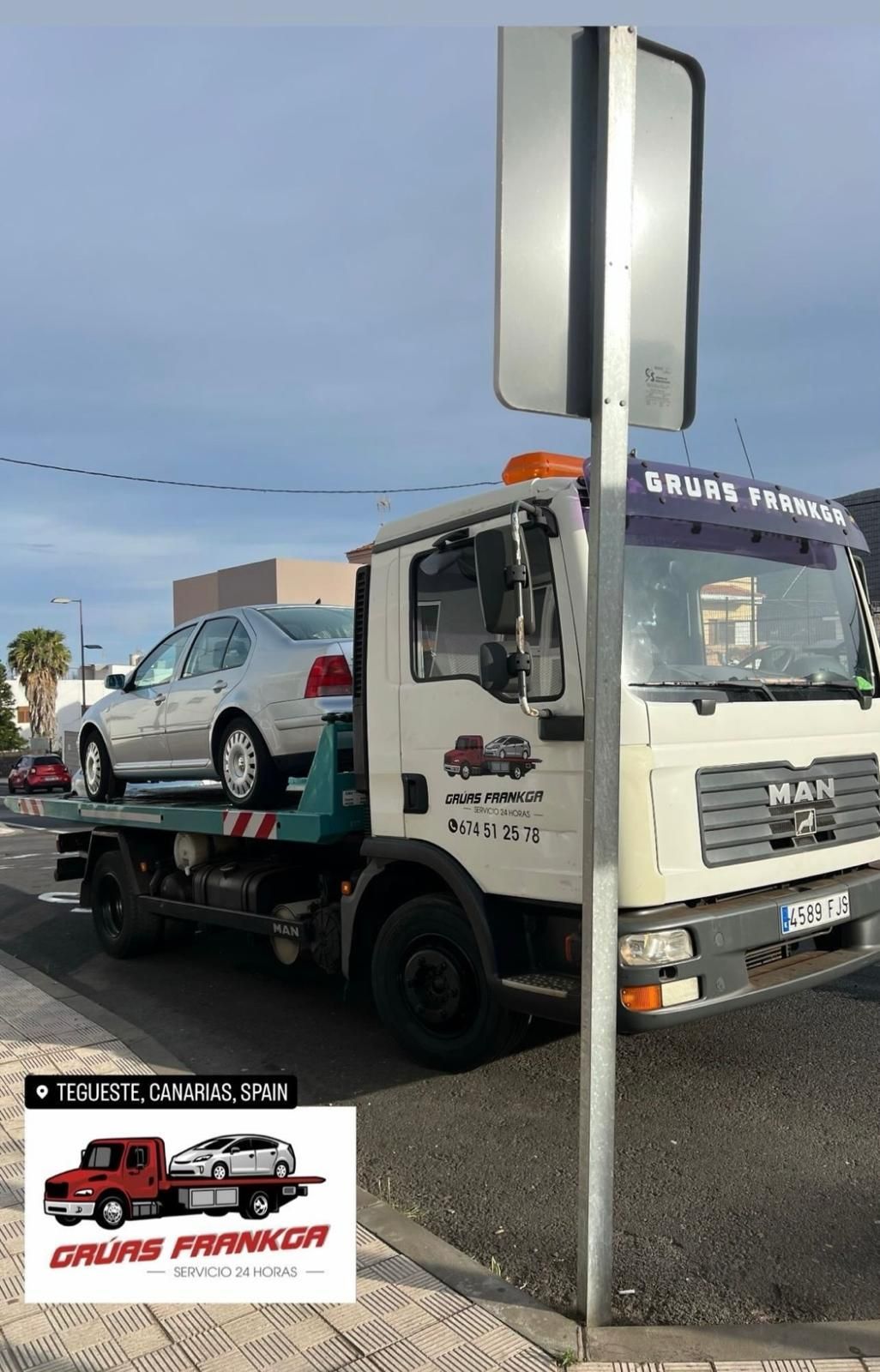Una grúa con un coche en la parte trasera está estacionada al costado de la carretera.
