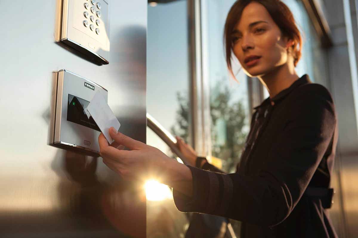 Une femme passe une carte d'identité dans un panneau d'accès de sécurité près d'une fenêtre.