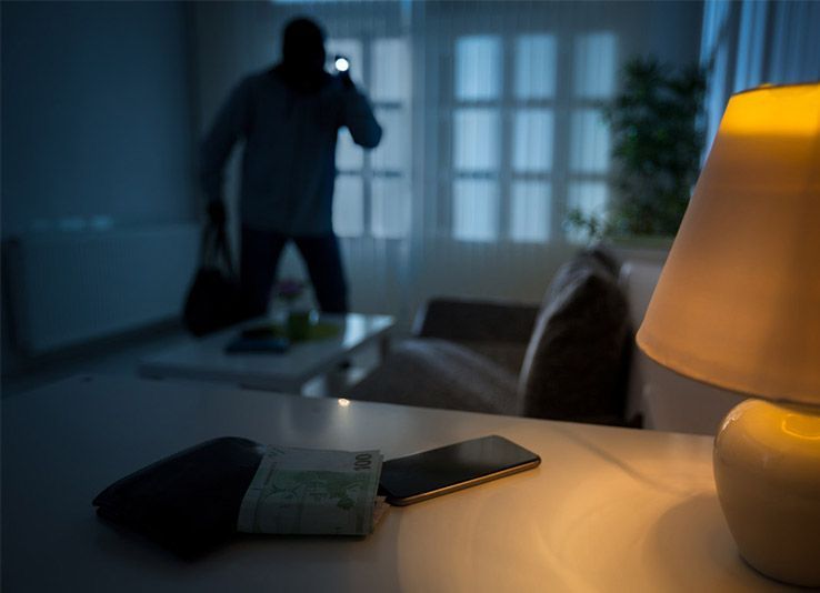Un cambrioleur avec une lampe de poche dans une pièce faiblement éclairée, une lampe éclaire une table avec de l'argent et un téléphone.