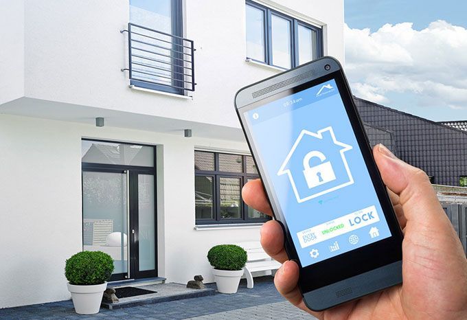 Main tenant un smartphone avec une application de sécurité à domicile, maison en arrière-plan.