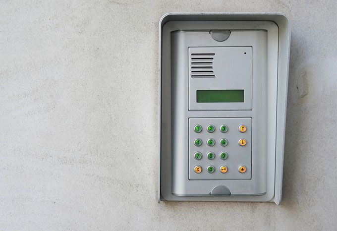 Système d'interphone gris avec clavier sur un mur blanc.