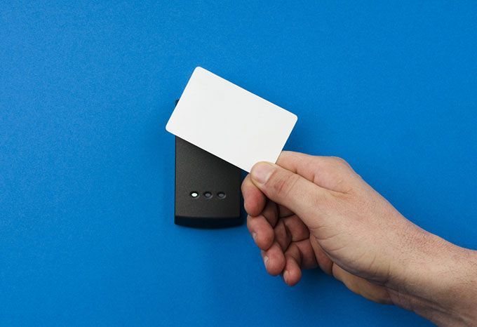 Main tenant une carte blanche sur un lecteur de carte noir sur un mur bleu.