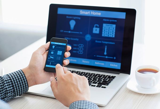 Personne utilisant un smartphone et un ordinateur portable pour contrôler une interface de maison intelligente ; écrans bleus.