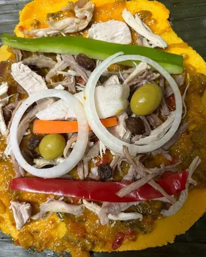 Primer plano de un tamal colorido y decorativo con pollo, verduras y aceitunas dispuestas como una cara sonriente.