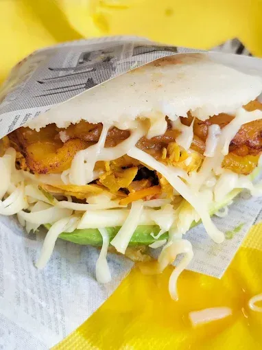 Arepa rellena de plátano, queso, aguacate y repollo, envuelta en papel amarillo.