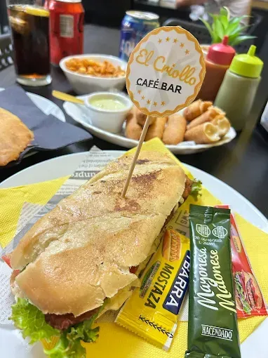 Sándwich en El Criollo Café Bar con guarniciones, condimentos y bebidas.