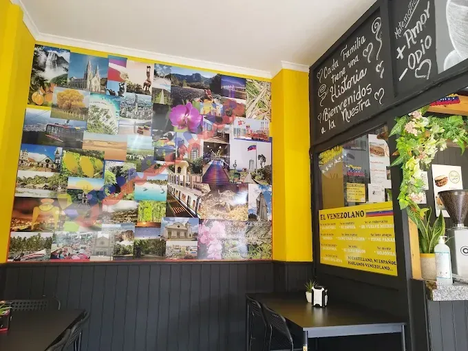 Interior de cafetería con una pared de collage de fotografías, molduras amarillas, mesas negras y un menú en la pizarra.