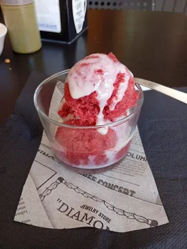 Una bola de sorbete rojo con un chorrito de blanco en un recipiente de vidrio sobre una servilleta, colocada sobre una mesa oscura.