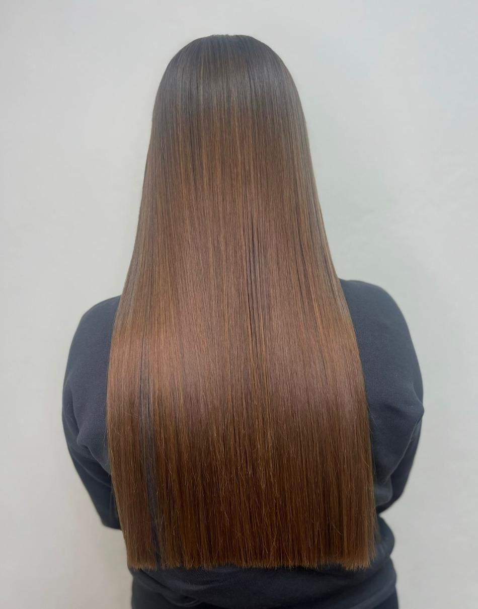 Cabello largo, liso y castaño de mujer cayendo en cascada por su espalda sobre un fondo claro.