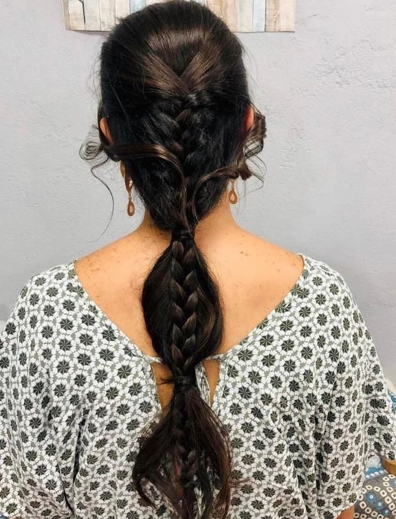 Cabello oscuro de mujer peinado en una trenza que se ensancha y luego se estrecha. Lleva un top estampado y pendientes.