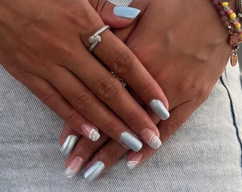 Manos con uñas de color azul claro y punta francesa, adornadas con un anillo y una pulsera, apoyadas sobre un denim claro.