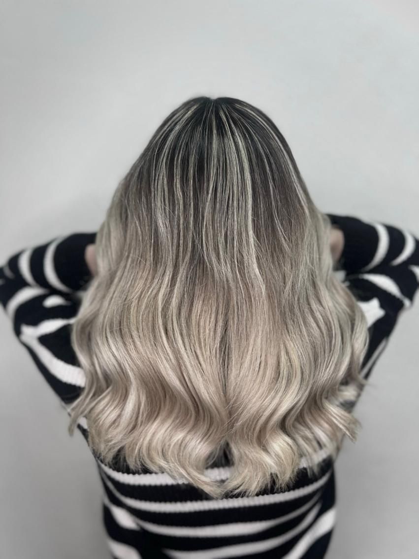 Cabello ombré: raíces oscuras que se desvanecen en ondas rubias claras. La persona lleva un suéter de rayas blancas y negras.