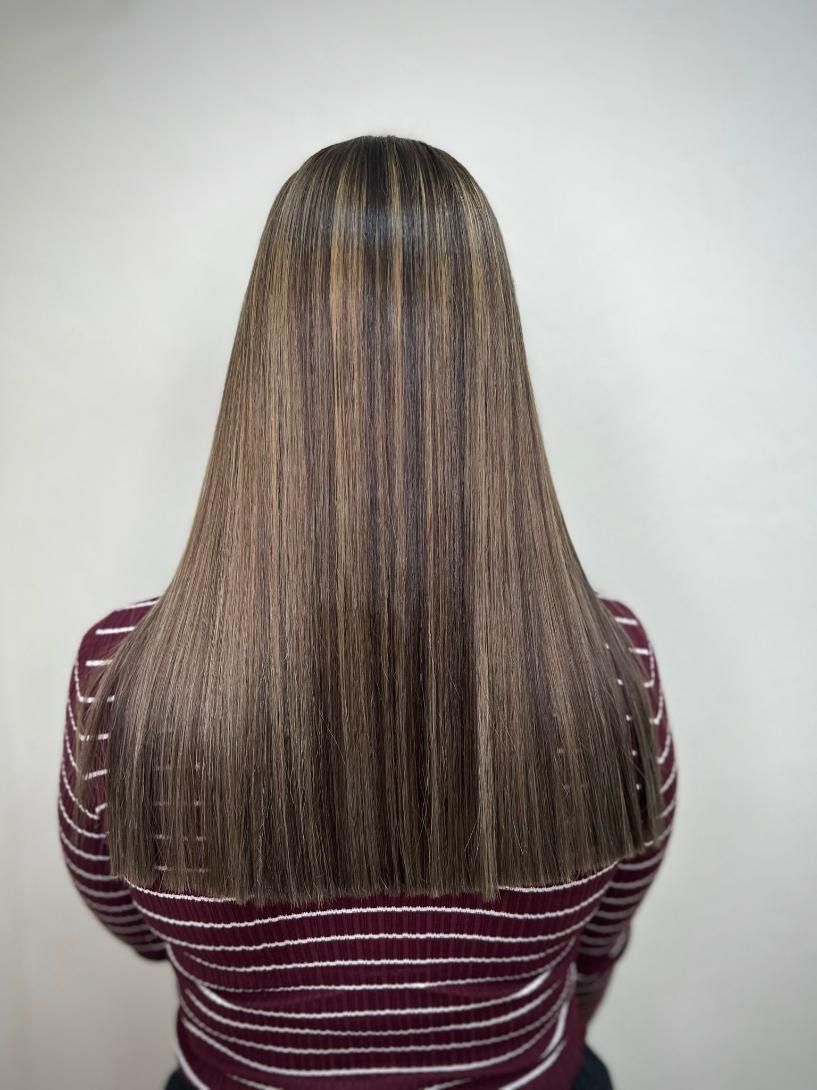 Mujer con cabello castaño largo, liso y con reflejos. Lleva una camisa de rayas color granate.