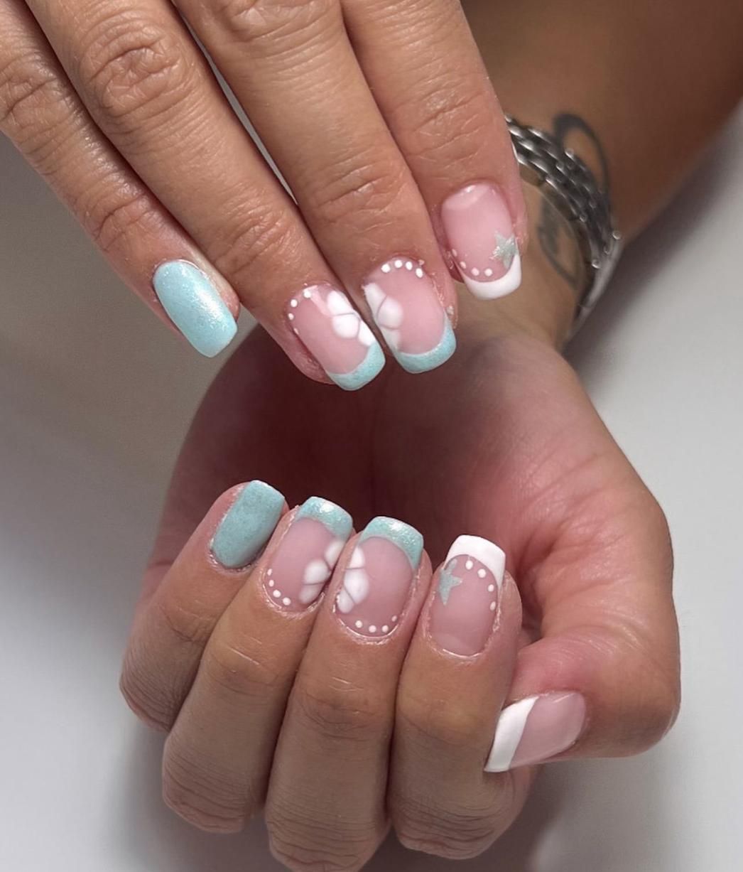 Manos con arte de uñas con punta francesa en tonos azul claro y blanco, con diseños florales y de puntos.