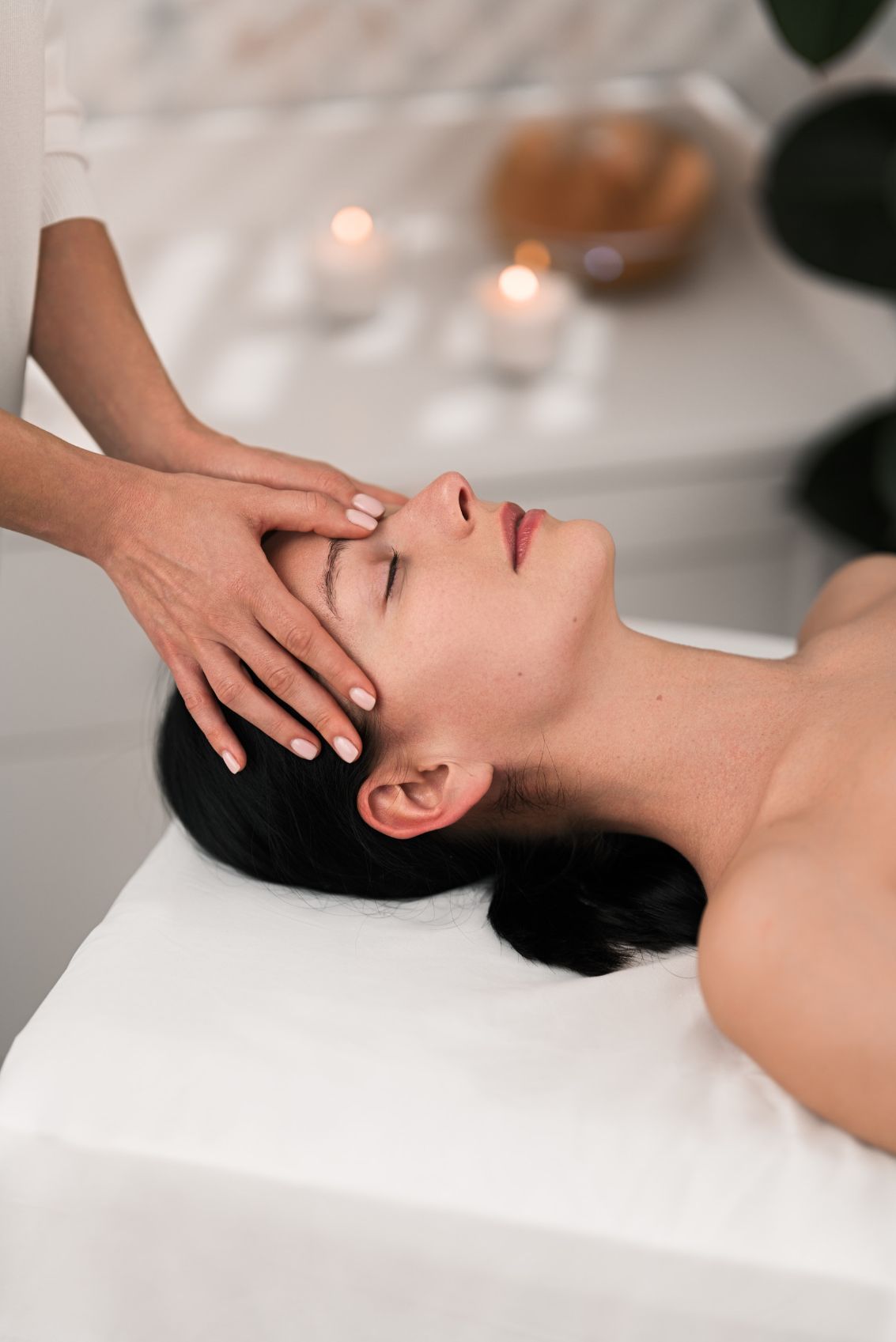 Mujer recibiendo un masaje facial en una camilla. Velas al fondo.