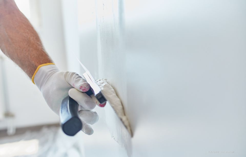 Eine Person trägt mit einem Spachtel Fugenmasse auf eine Gipskartonfuge auf.