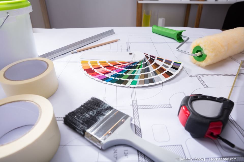 Malutensilien auf Architekturplänen: Farbmuster, Pinsel, Farbroller, Klebeband und Messwerkzeuge.